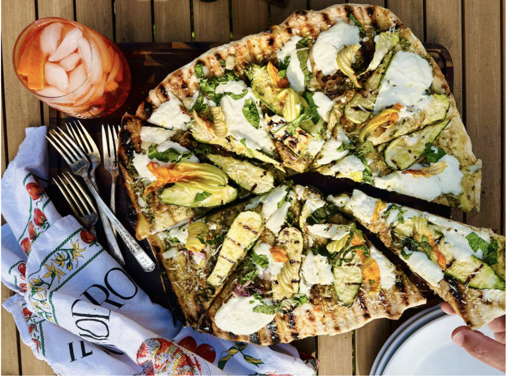 Pizza with grill marks rounds of white cheese and yellow zucchini flowers
